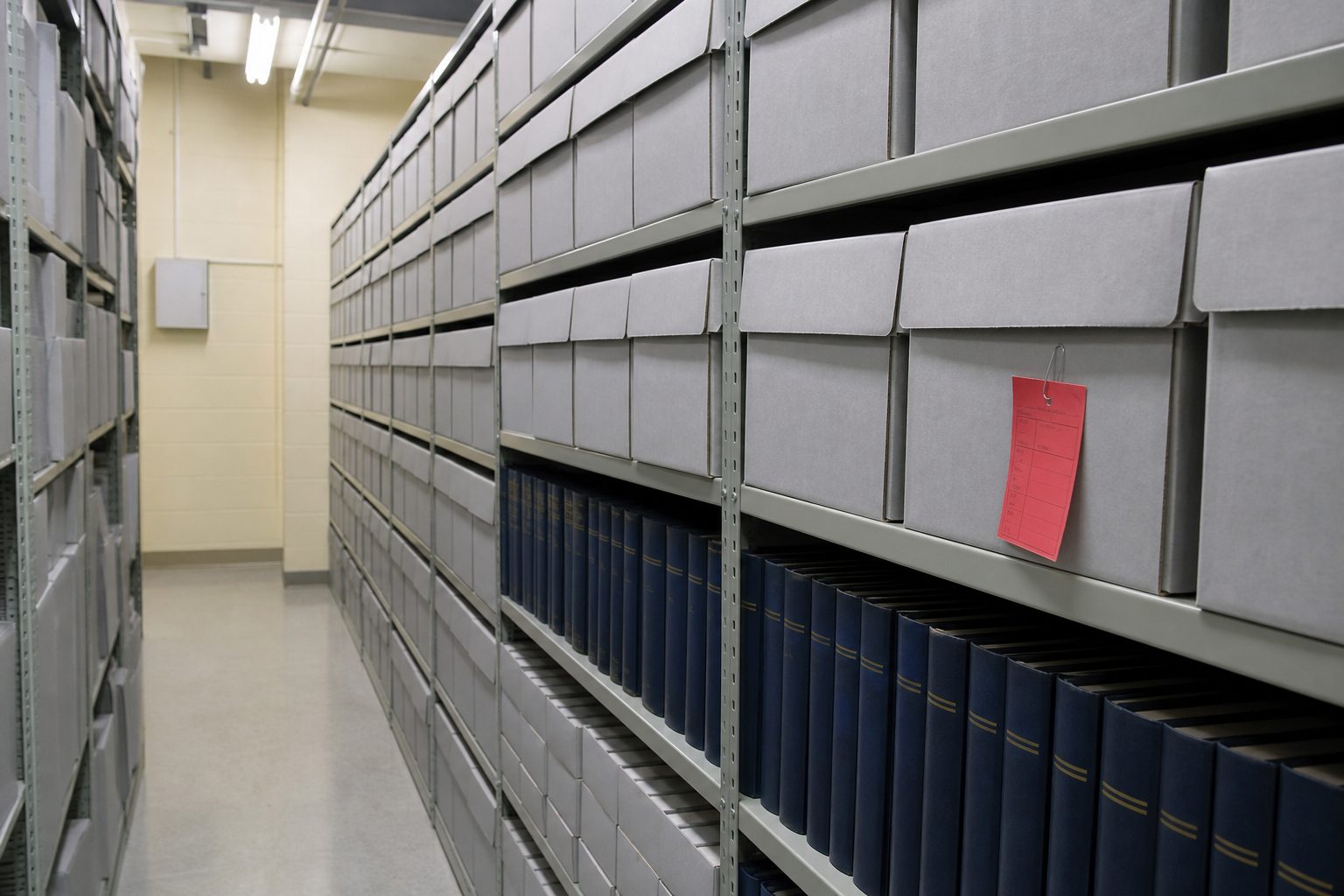 Municipal records room aisle with gray archive boxes on steel shelving and bound minute books